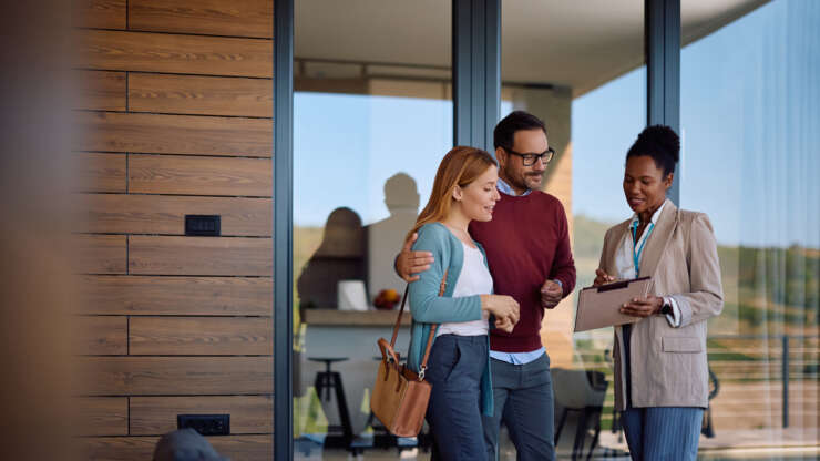 Smiling couple and their real estate agent analyzing paperwork during open house day.